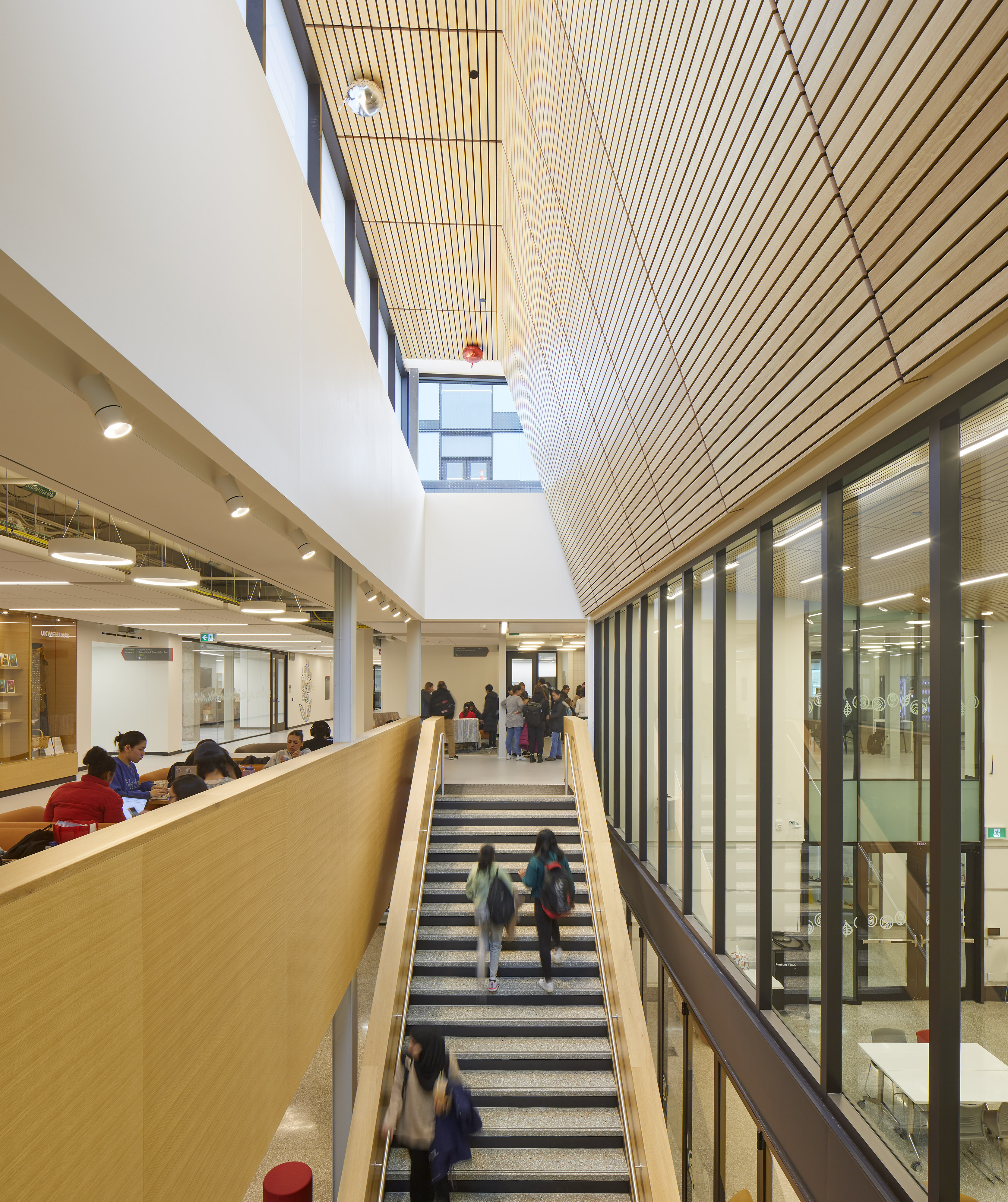 Students milling about the campus with a focus on a large staircase and wooden architectural features.