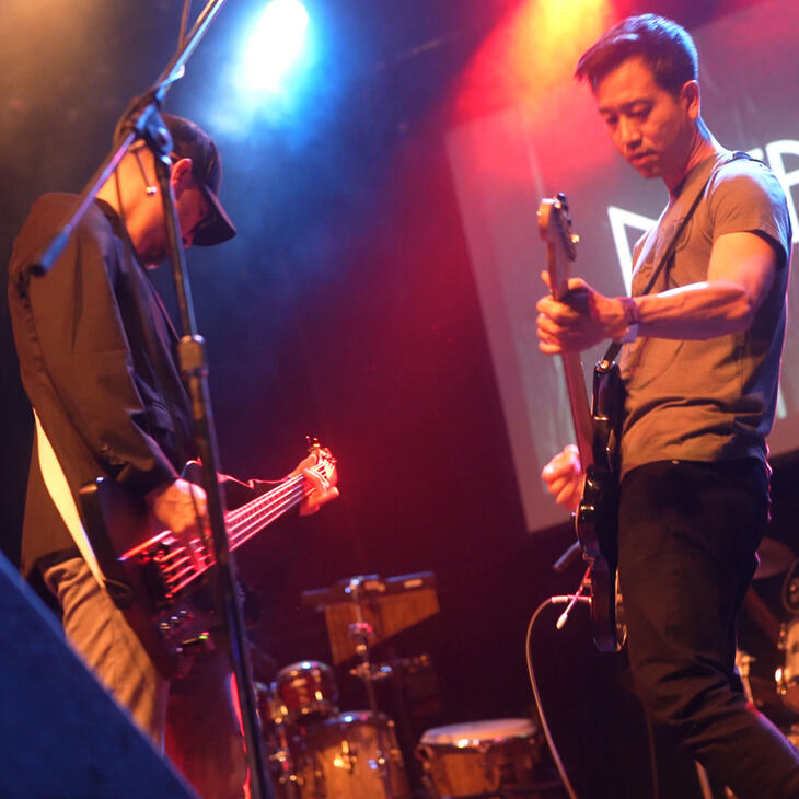 Two guitarists face each other while performing on stage at Eco Jam.