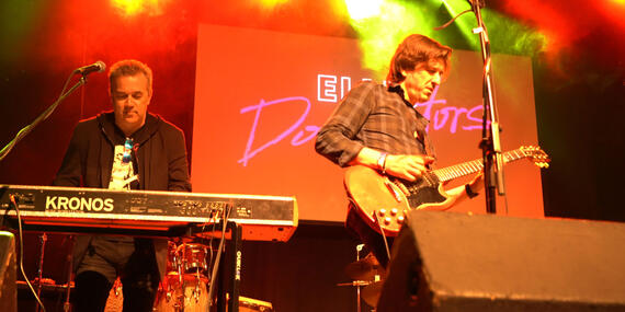 Guitarist and keyboard player play on stage. "EllisDominators" sign in background.