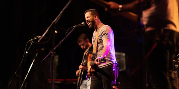 Side shot of singer yelling into microphone in foreground, with bassist playing in the background.