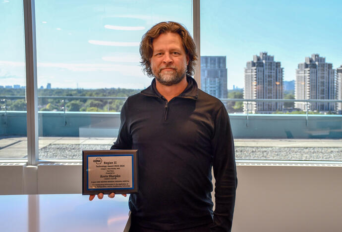 Man in front of a window holding a plaque for the 2024-2025 ASHRAE Technology Awards.