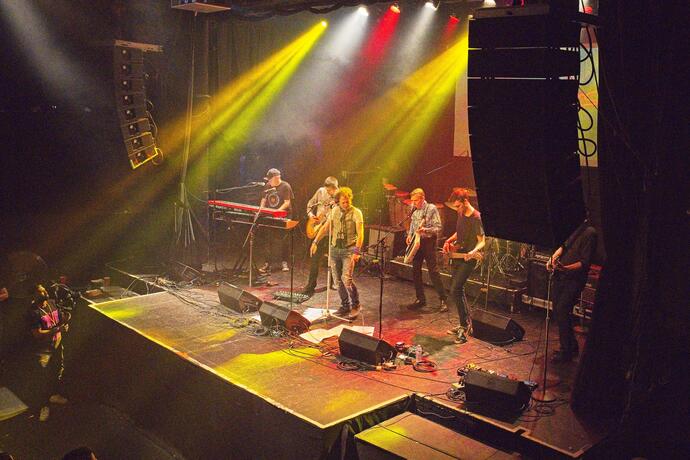 Far away shot of a band playing on stage with yellow stage lights. 