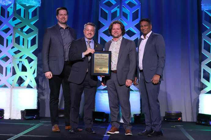 Man presenting award plaque to three other men, posing for an image