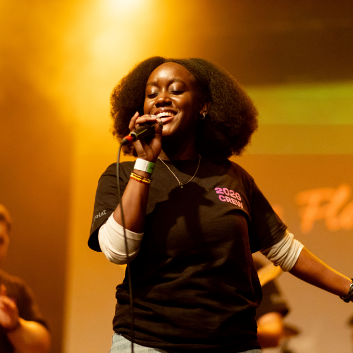 Performer holding a microphone on stage under warm yellow lighting.